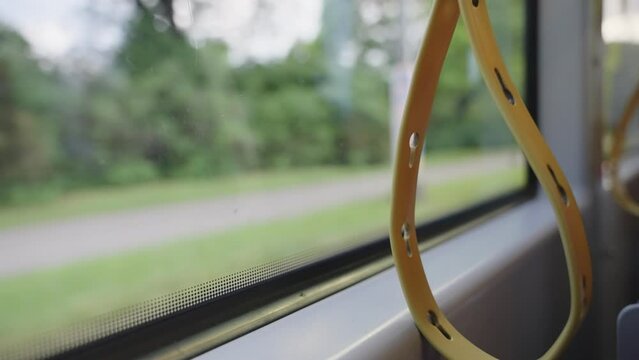 Grab handles straps for standing passengers on public bus straphangers standees. Yellow straps for holding during public transport bus train or tram ride. Street pass by at the window of European bus