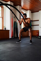 Determined young black man doing battle ropes exercises at the gym