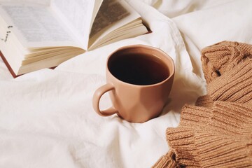 Open book, cup of aromatic coffee and woolen brown sweater. Warm and cozy home. Vintage autumn and winter background