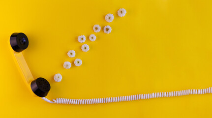 The handset of a yellow retro phone on a yellow background. White flowers come out of the handset of the phone. The concept of love, romance and Valentine's Day. Banner with a space for text