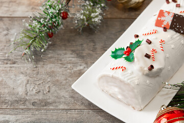 White chocolate yule log cake with christmas ornament on wooden table. Copy space