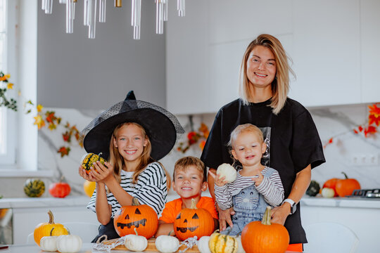 Mom with three young kids in halloween costumes are posing on the kitchen