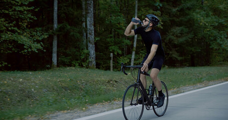 CU Cyclist drinking water while cycling on an empty forest road