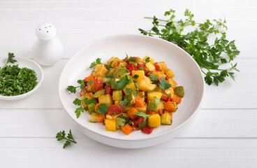 Vegetable stew with zucchini, carrots, potatoes and parsley on a white plate on a light gray background
