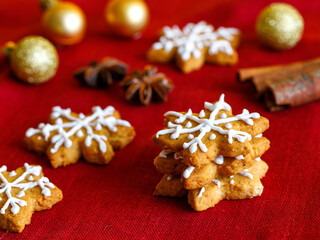 Homemade gingerbread cookie in shape of snowflakes decorated with icing on red napkin with anis star, cinnamon stick and golden ball. Traditional Christmas food. Christmas and New Year holiday concept