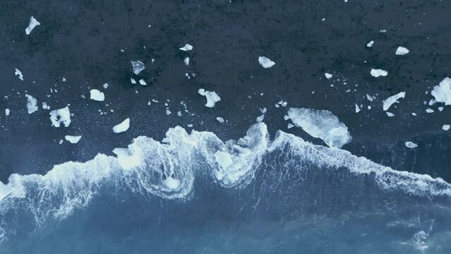 Waves Crashing On Iceberg Fragments Scattered On The Black Sand Of Diamond Beach In Iceland. - aerial
