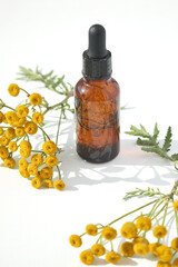 An empty mock-up of a medical bottle with a pipette and aroma oil. Transparent bottle made of dark amber glass with a green plant and yellow flowers. The concept of phytotherapy and aromatherapy