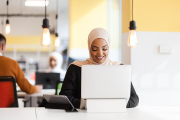 African american muslim girl with hijab working on a laptop in an office..