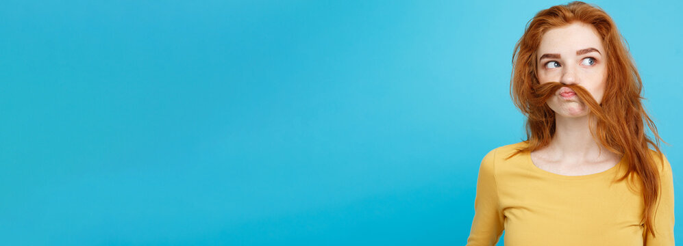 Headshot Portrait Of Happy Ginger Red Hair Girl Imitating To Be Man With Hair Fake Mustache. Pastel Blue Background. Copy Space.