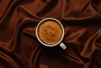 Cup of coffee on brown smooth silk fabric, top view, aesthetic minimal concept