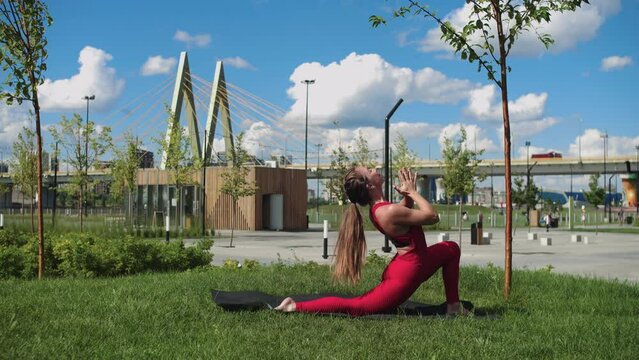 An adult woman with nice body doing meditative exercises in the park by the bridge