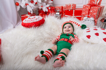 Newborn baby girl dressed in gnome costume lying on white fur carpet among christmas decorations....