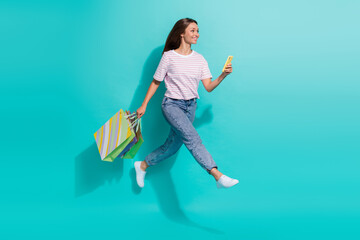 Full size photo of positive cheerful woman flying jumping hold smartphone shopping bags look empty space isolated on teal color background