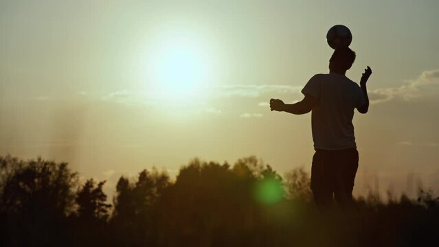 Silhouette of a man kicking the ball with his feet and head. Slow-motion video of outdoor soccer training. Beautiful nature, sunset and a person actively engaged in sports. High quality 4k footage