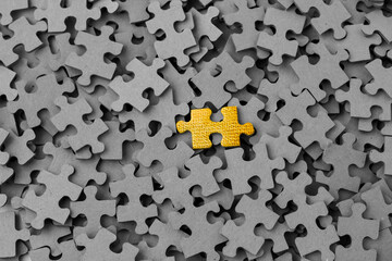 A yellow puzzle piece on top of many cardboard puzzle pieces with the back turned