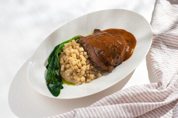 Traditional German braised beef cheeks in brown red wine sauce with celery risotto on white...