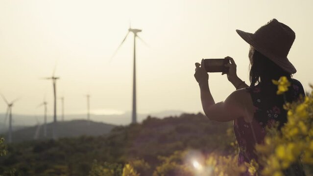 A girl takes pictures of windmills in the mountains at sunset. Renewable energy, production of electricity from wind turbines. High quality 4k footage