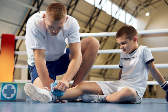 Personal coach, team trainer provides first aid to an athlete with a leg injury. Boxing training in the gym. Sport, medicine, studying