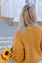 A girl in a knitted sweater with a wicker bag with sunflowers crosses the road on a pedestrian crossing.