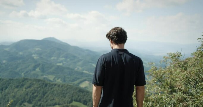 Man, wearing dark shirt, looking ito the valley from peak of the mountain.