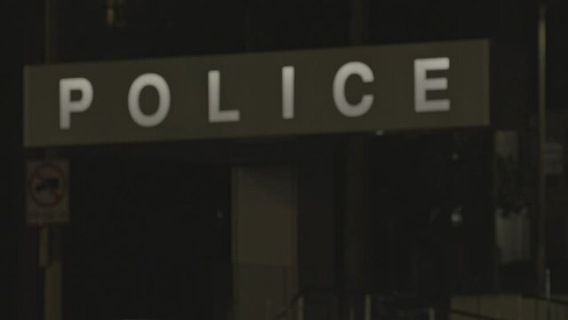 A static shot of a facade side of a police station where one board is seen written police on to it at night