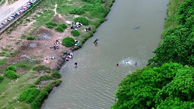 Aerial top down of Haitian kids swimming in dirty river and adults washing clothes - poor country of Haiti 