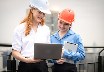 Engineer man and architect coworker standing outdoors on rooftop of construction site looking at blueprint for apartment, housing development. Maintenance building contractor discussion with teamwork