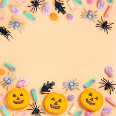 Halloween sweet background frame with scary pumpkin cookies, candy and Halloween decor on orange table