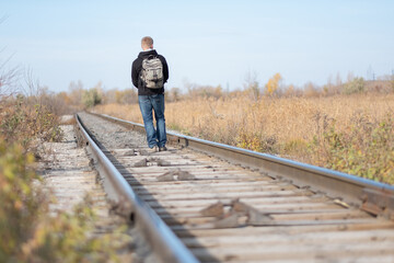 a man with a backpack on his back walks along the rails. hike. walk on the rails.traveler on the railroad