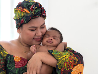 Close up, mom holding cute little baby boy. Asian mother wearing colorful African traditional clothes.