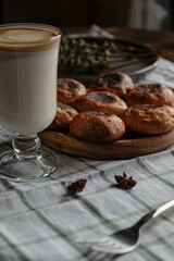 Scones on a wooden plate with fork, coffee and milk in a glass cup. On a white checkered towel