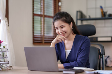Attractive Asian businesswoman using laptop in office Take notes of work details, smile brightly.