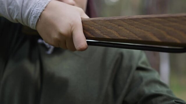 Girl in old styled clothes presses trigger of wooden crossbow in spring forest closeup. Camp of roleplayers. Medieval armour for teenagers training