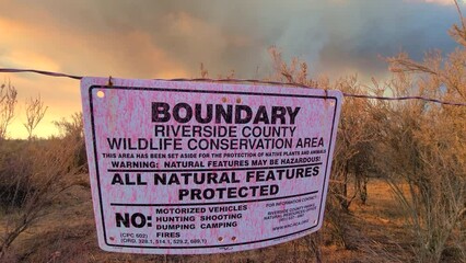 Conservation boundary sign blows in wind as large wildfire burns in the background