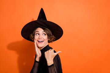 Photo of dreamy excited girl dressed black gothic dress headwear looking back pointing empty space isolated orange color background