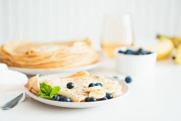 French crepes with banana and blueberries on white table. Copy space