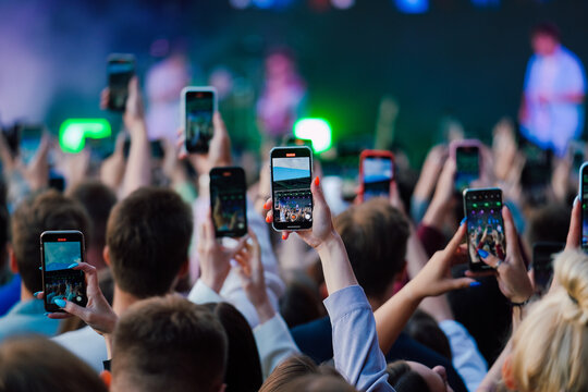 Hands raised up with smartphones recording videos of the music performance on a stage 