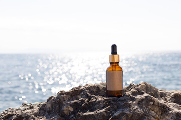 A bottle of serum on the rocks against the sea. A mock-up for a cosmetic product. Skin care essence...
