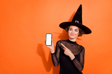 Portrait of attractive enchant lady look indicate finger empty space phone display isolated on orange color background
