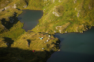 Aerial view of a lot of tents on the shore of a mountain lake. Hiking and camping in the mountain side.