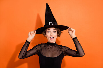 Photo of sexy impressed young lady wear black witch dress hands cap open mouth isolated orange color background