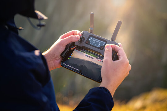 Close up view of a drone radio remote controller in a male photographer hands while taking pictures and videos of a beautiful mountain landscape during sunrise.