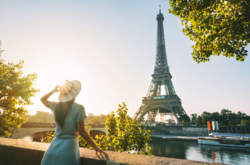 Rear view of woman tourist in sun hat standing in front of Eiffel Tower in Paris at sunset. Travel...