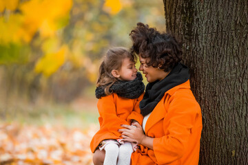 Mom and daughter in orange coats are walking and laughing in the park on a warm day. Family values - spending time with children, taking care of health and walking.