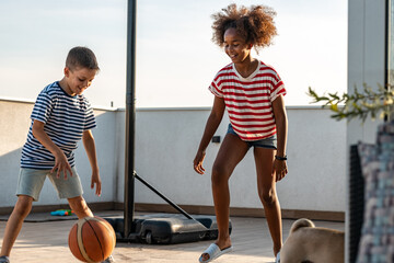 Caucasian boy and african girl playing outdoors basketball 