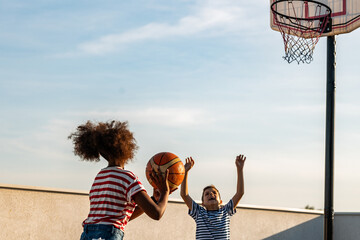 Caucasian boy and african girl playing outdoors basketball 