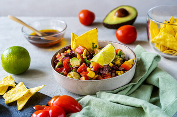 Cowboy caviar is traditional Mexican vegetable salad in bowl with ingredients and nachos on concrete background 