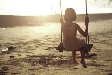 Rear view of lonely Asian girl sits on the wooden swing with sunset in background
