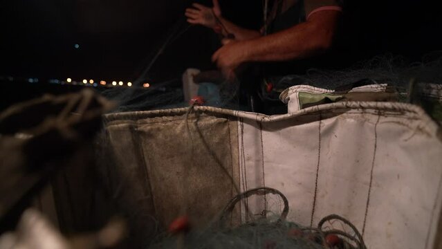 Low angle view from a basket as a fisherman pulls fish netting out to set at night.