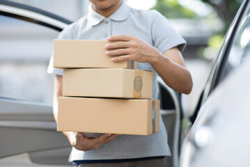 A delivery man is delivering cardboard boxes to customers at the door of a private car. young man...